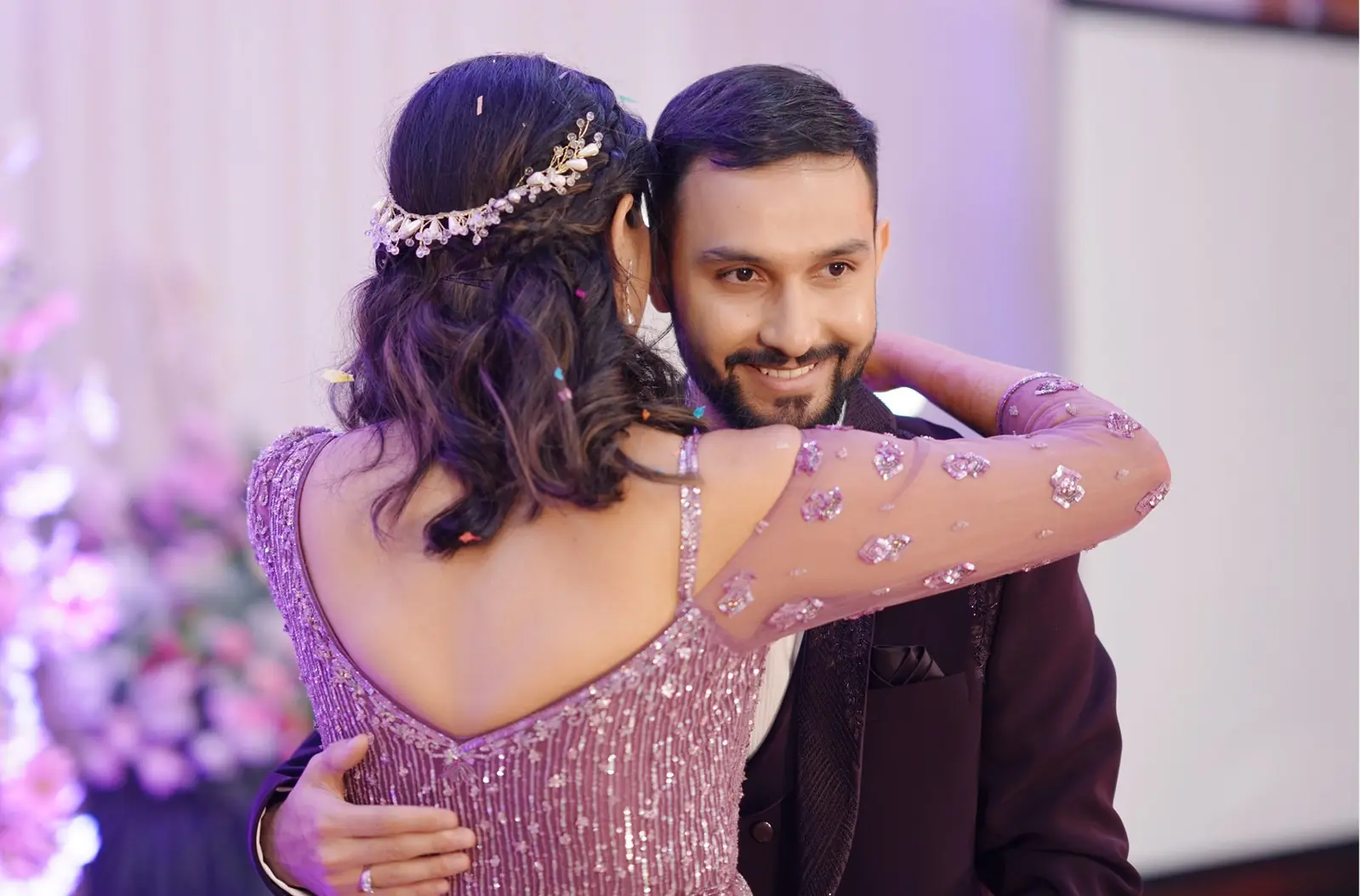 Couple embracing at a wedding reception. Bride with beaded headpiece and groom in a suit smiling.